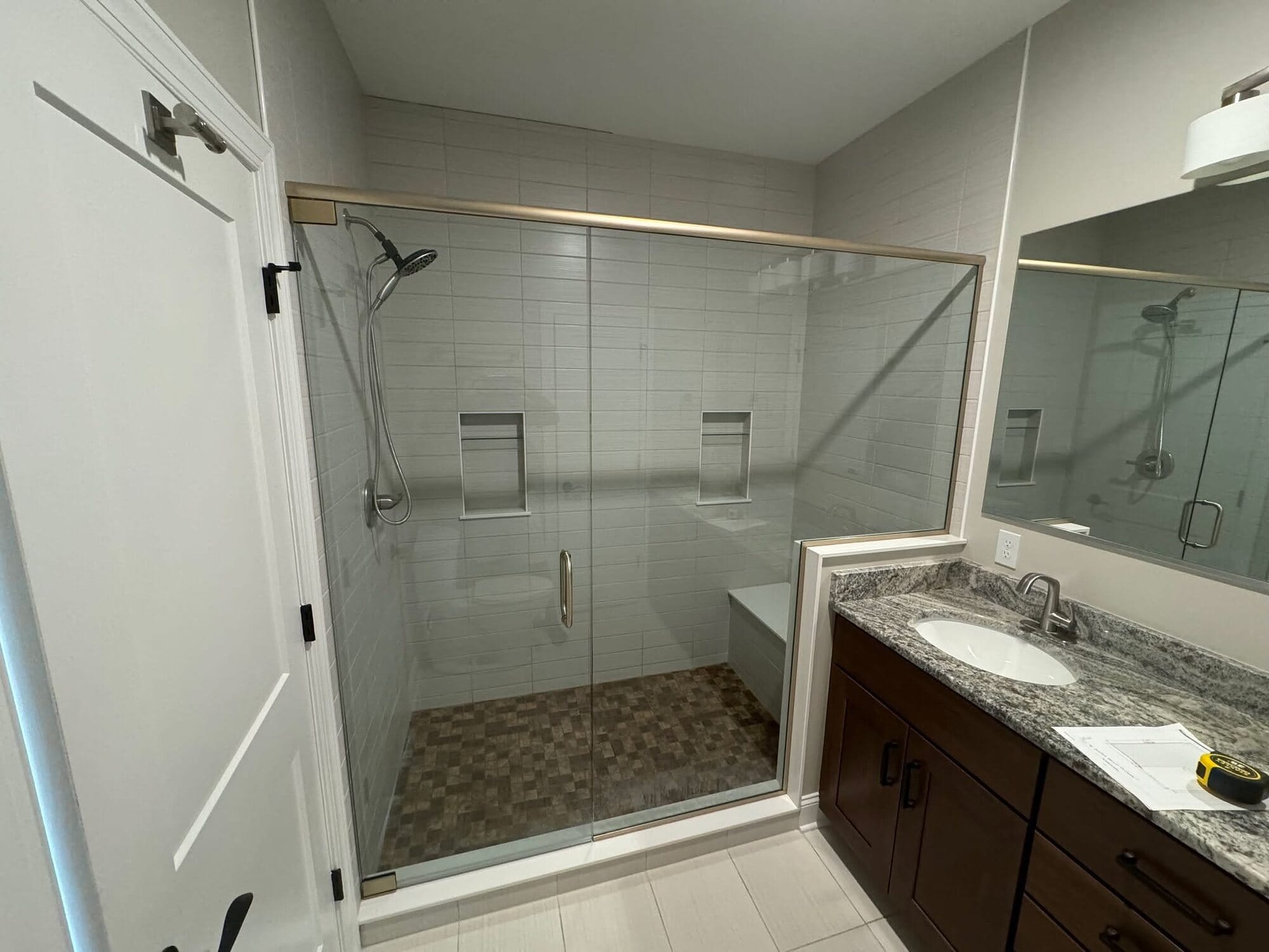 Bathroom with a tile walk-in shower behind a sliding glass door, mosaic shower floor, and a stained wood vanity.
