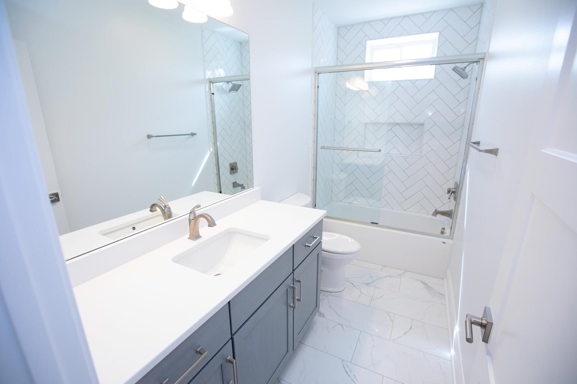 Bathroom with a gray vanity and white quartz top, framed mirror, and a glass-enclosed tub and shower combination.