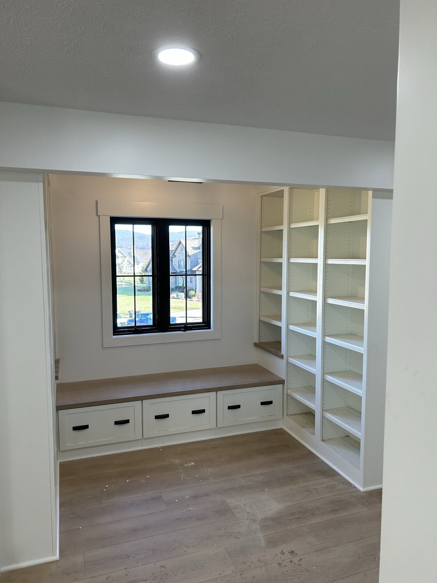 Custom closet built-ins in white with a cushioned window seat, drawer storage below, and floor-to-ceiling adjustable shelving.