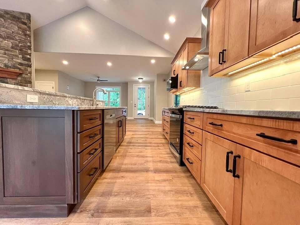 Kitchen with cherry stained cabinetry, granite countertops, a stone fireplace, vaulted ceiling, and hardwood flooring.