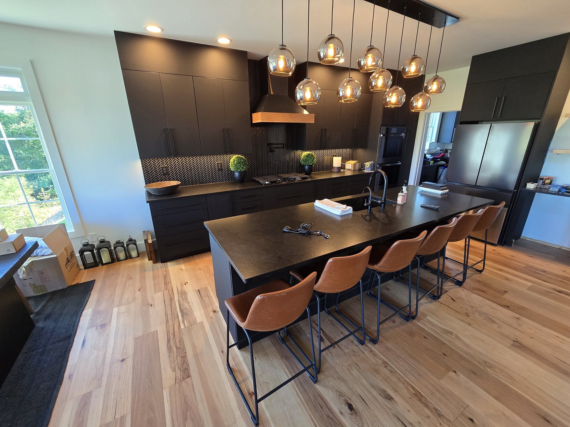Open-concept kitchen with dark flat-panel cabinetry, an extended island with leather counter stools, and a cluster of glass globe pendants.