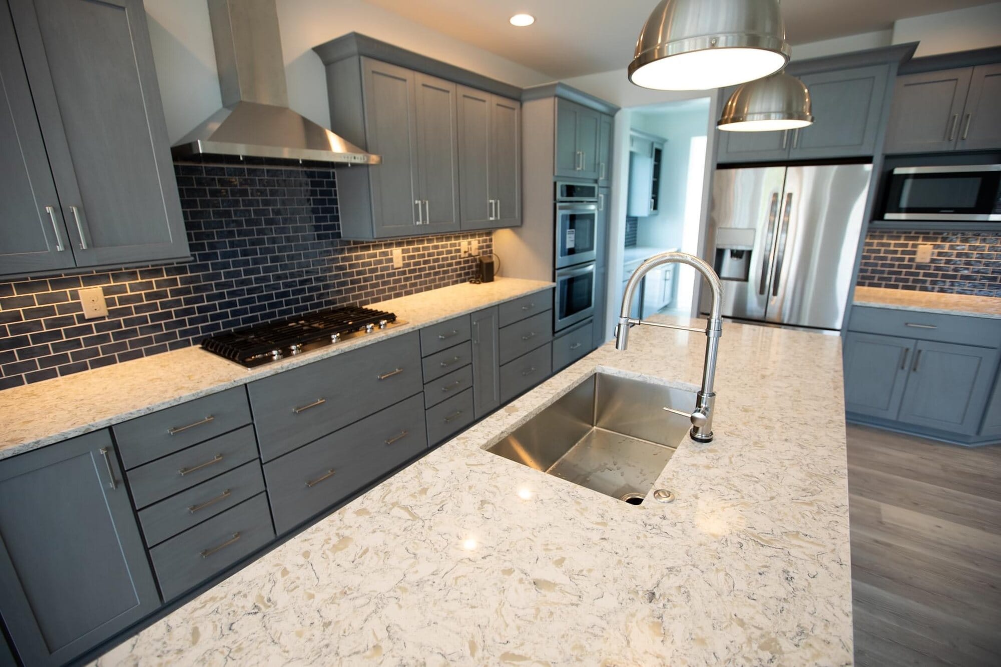 Kitchen featuring gray shaker cabinets, granite countertops, a dark subway tile backsplash, stainless hood, and undermount sink.