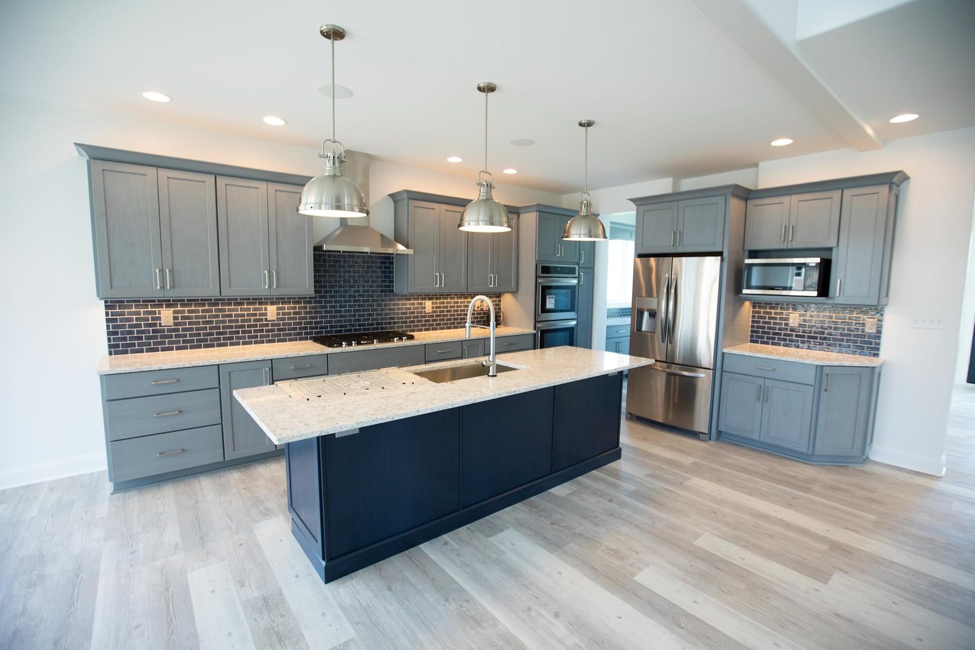 Kitchen with gray perimeter cabinetry, a navy island, quartz countertops, mosaic tile backsplash, and pendant lighting.