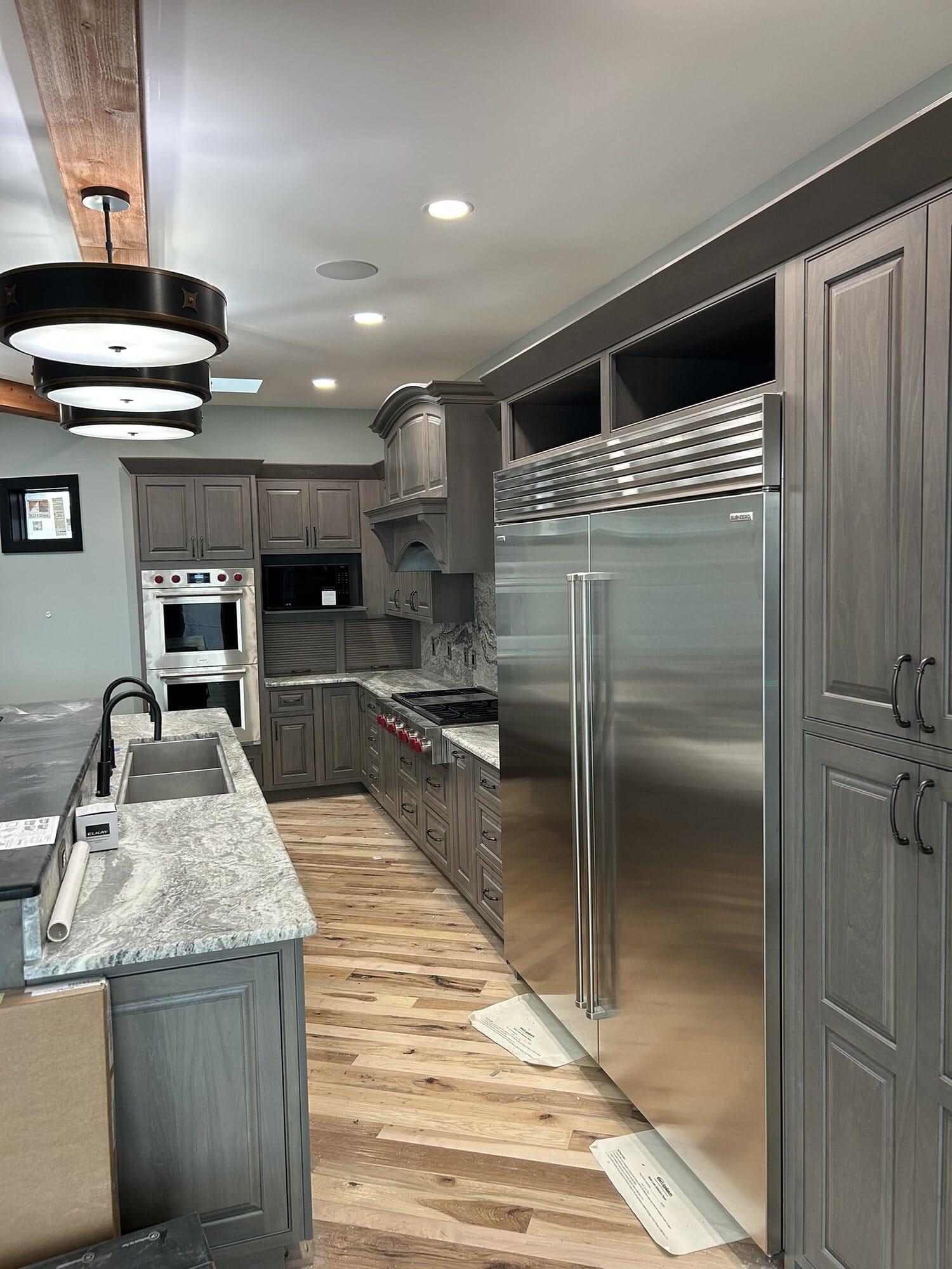 Kitchen with a panel-ready built-in refrigerator, double wall ovens, gray stained cabinetry, and hickory plank flooring.