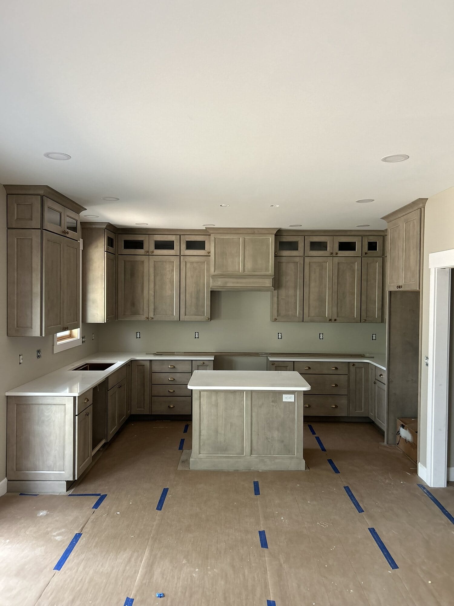 Newly installed gray stained kitchen cabinetry with glass-front uppers, center island, and crown detail ahead of final finishing.