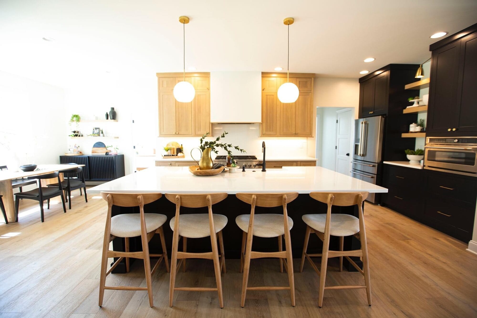 Kitchen featuring a white oak island with seating for five, dark perimeter cabinetry, brass open shelving, and globe pendant lights.