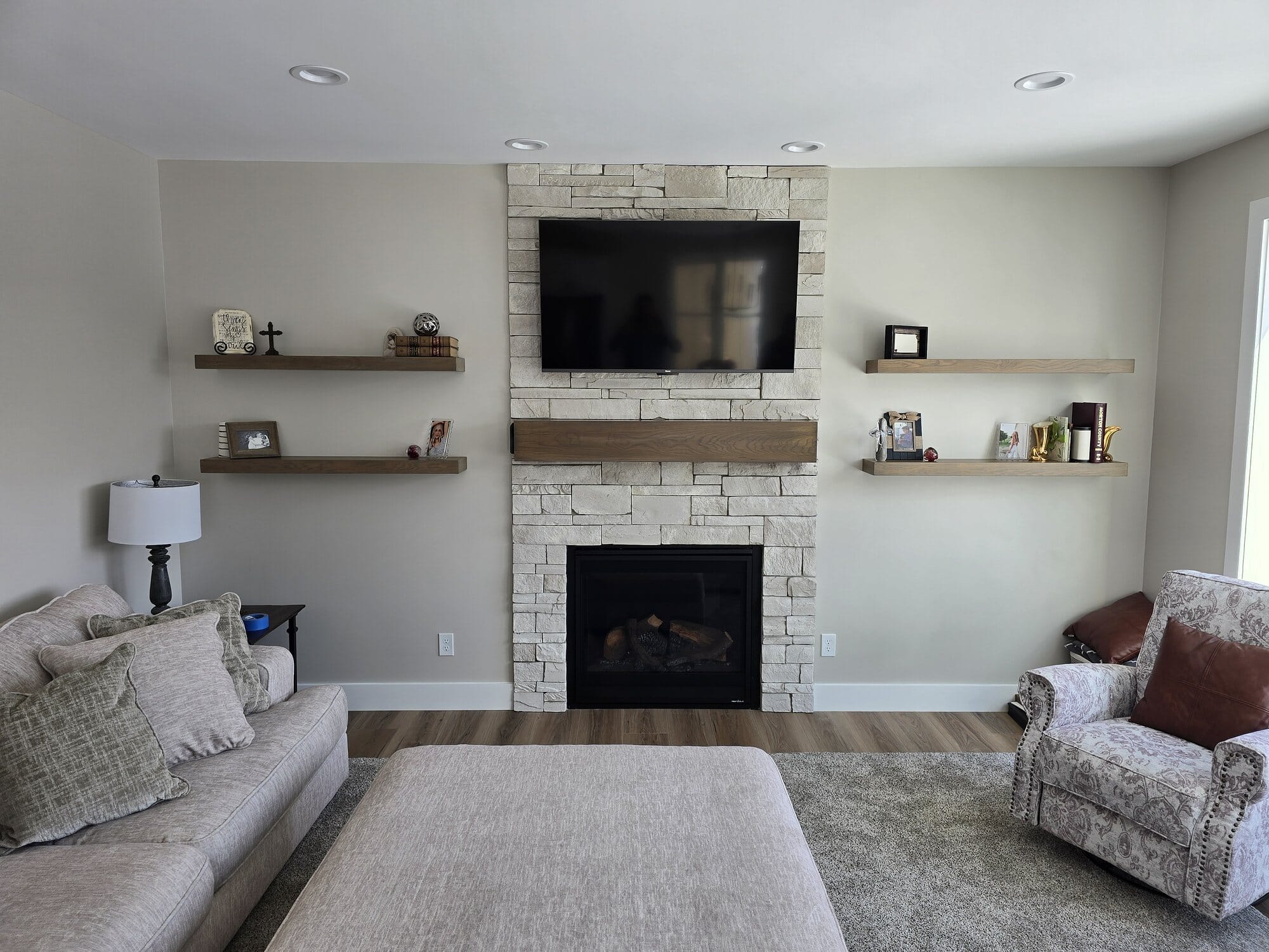 Living room featuring a stacked stone fireplace surround with mounted TV and custom floating wood shelves flanking the hearth.