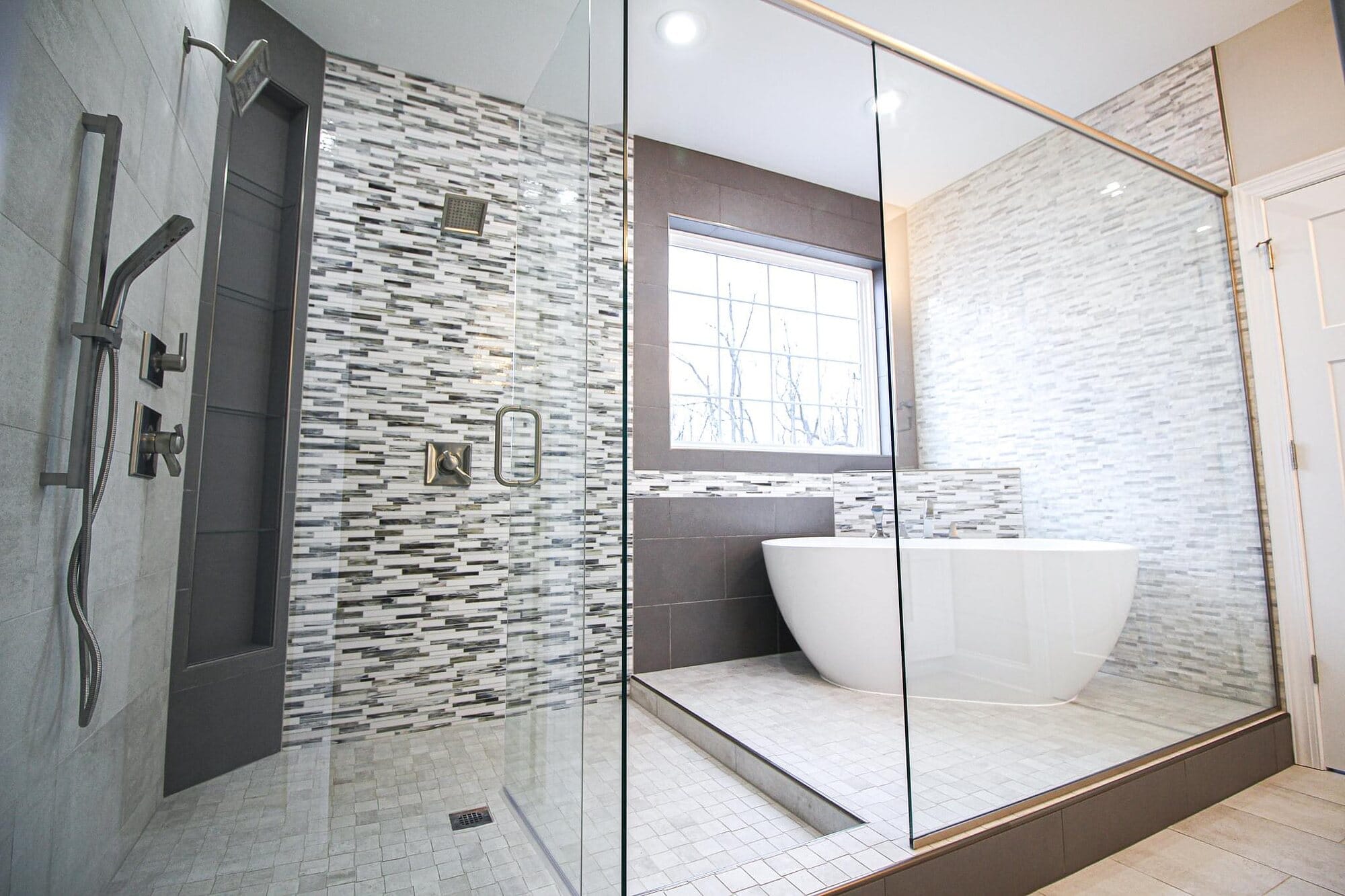 Master bathroom with a freestanding soaking tub, frameless glass shower enclosure, and a linear mosaic tile accent wall.