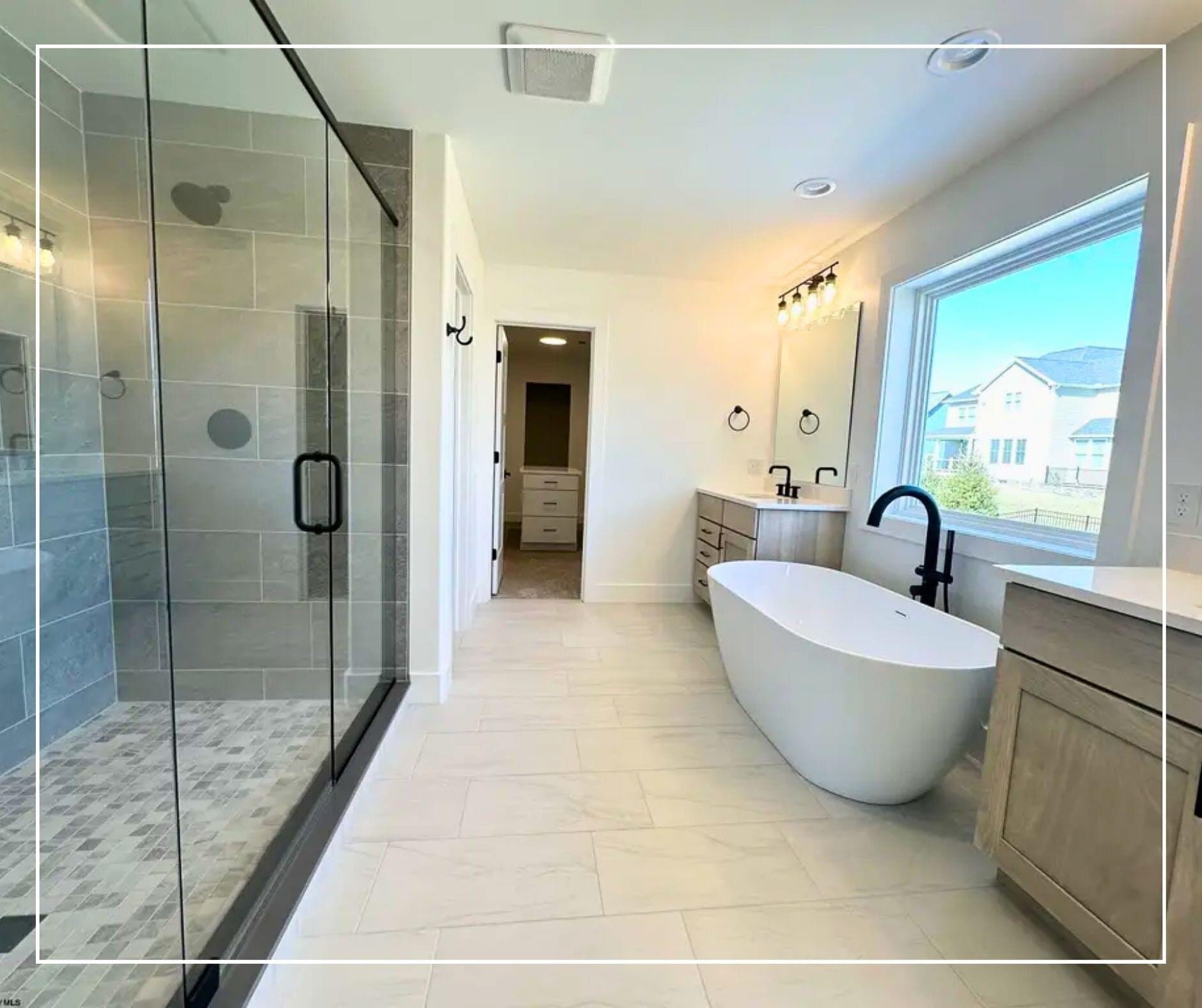 Master bathroom with a frameless glass shower, freestanding soaking tub, oak double vanity, and large-format tile flooring.
