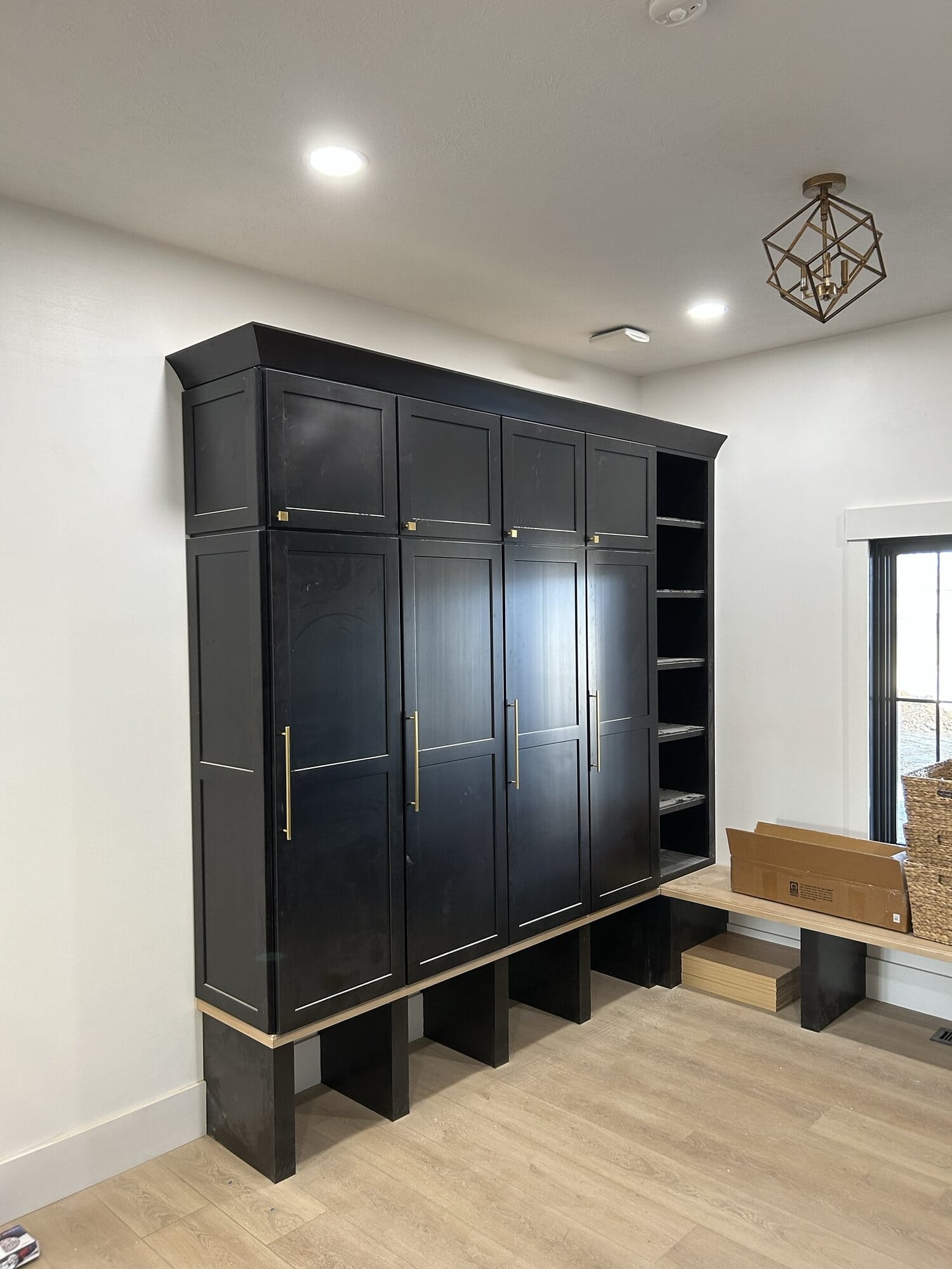 Mudroom featuring tall black locker cabinets with brass hardware, open lower cubbies, and a wood bench seat.