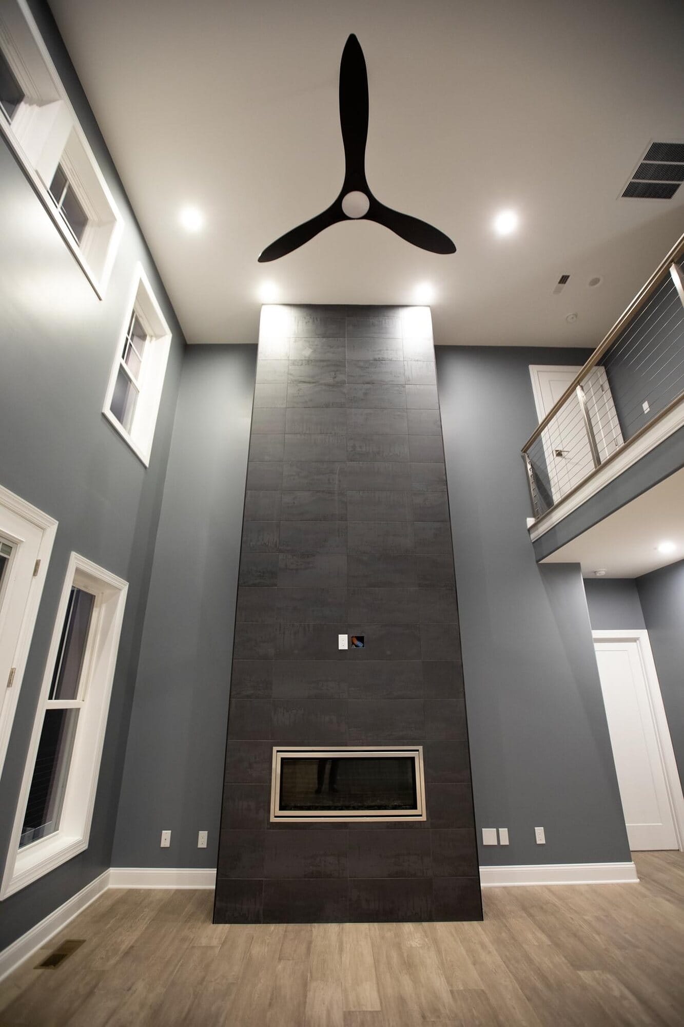 Two-story great room fireplace clad floor to ceiling in dark tile with a linear gas insert and cable-rail loft above.