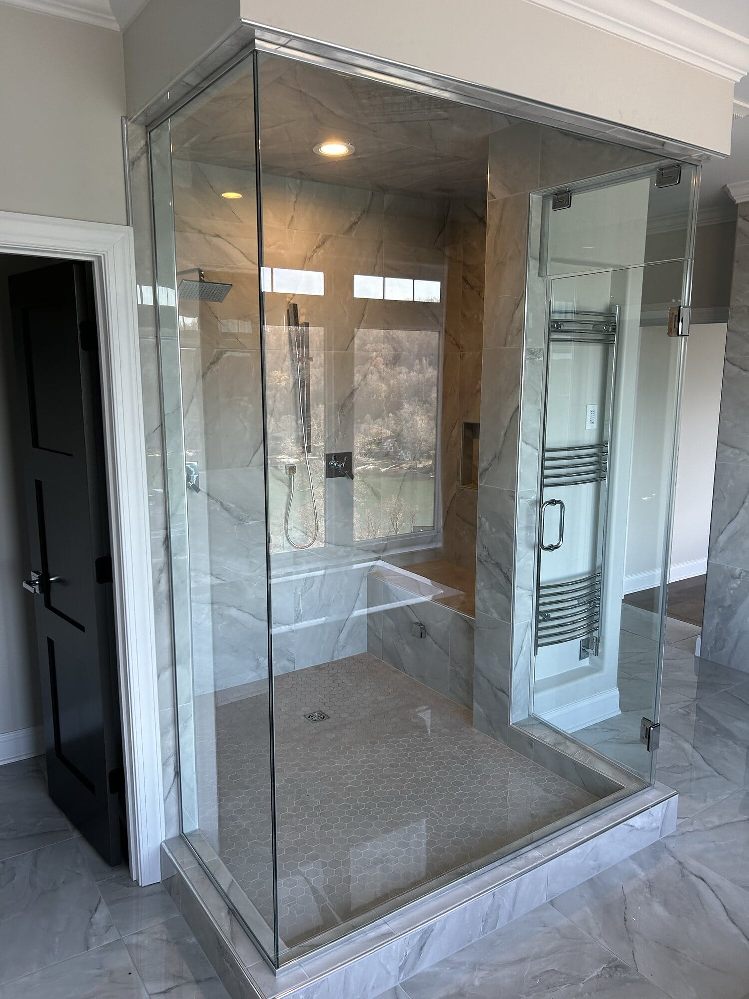 Frameless glass walk-in shower finished in marble-look large-format porcelain tile with a built-in bench and niche.