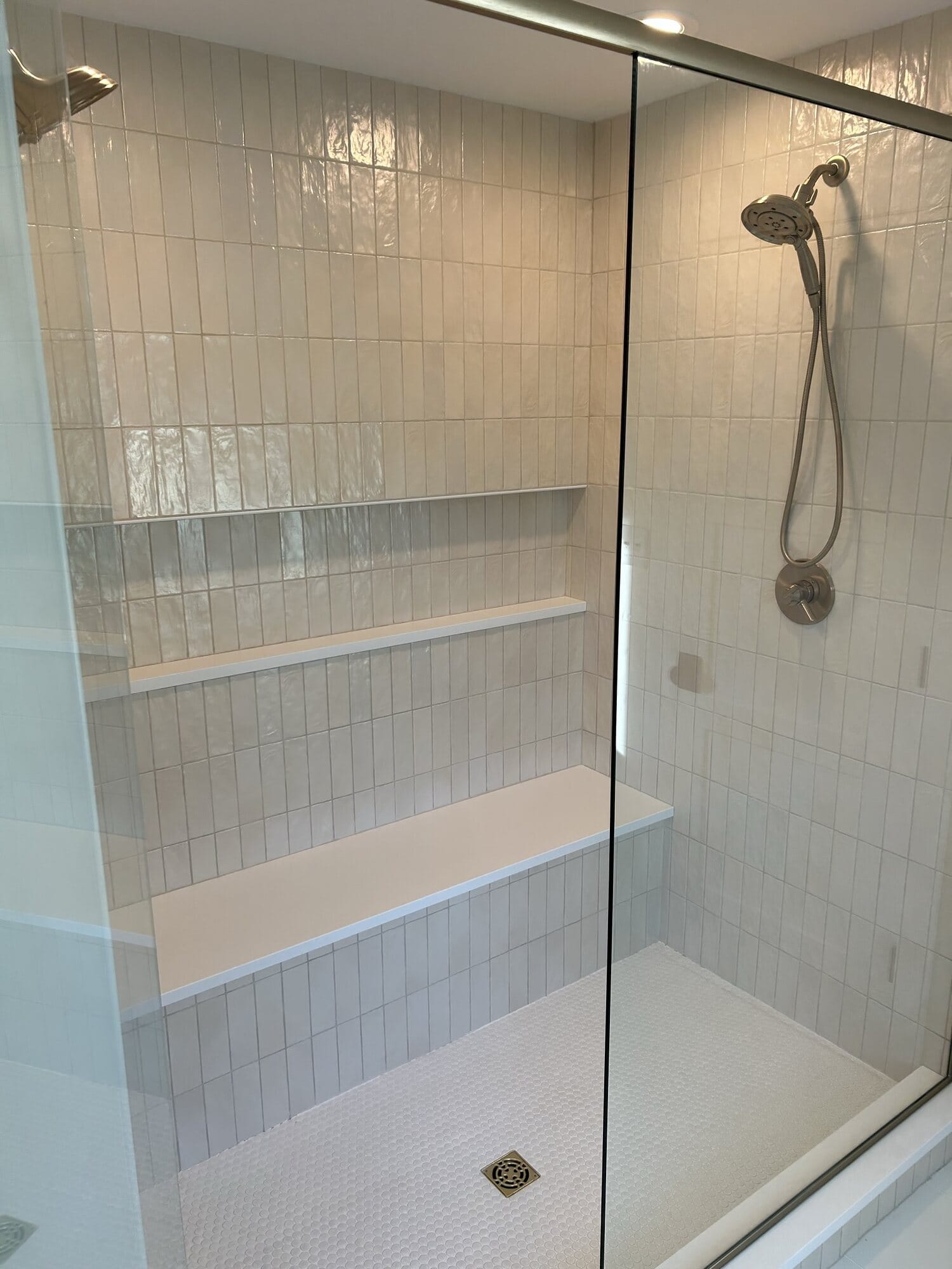 Walk-in shower with vertically stacked white tile, a full-width bench, recessed shelf niche, and framed glass door.