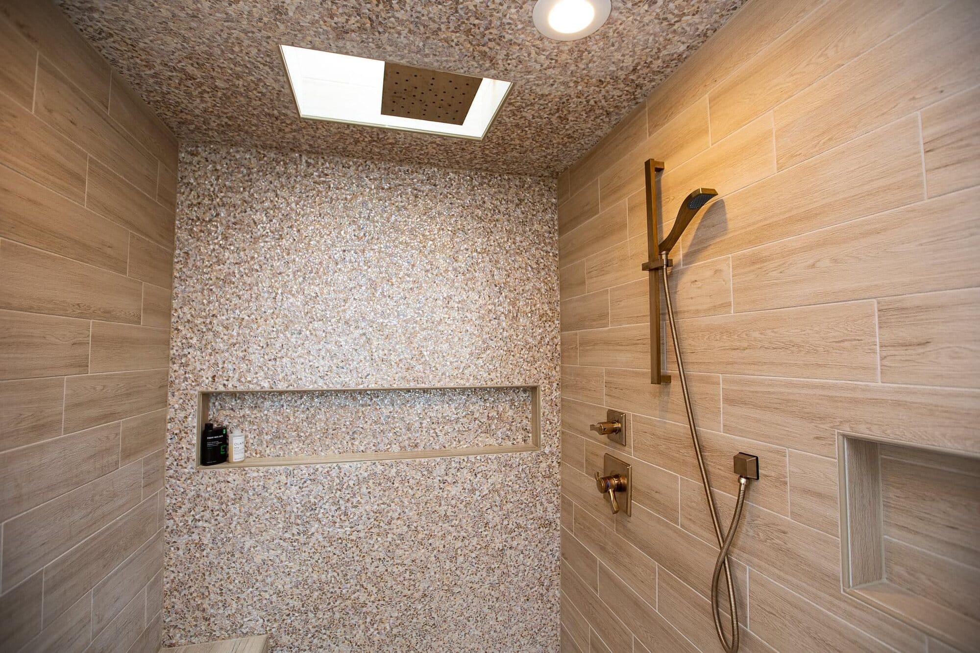 Walk-in shower with wood-look plank tile walls, a pebble mosaic ceiling and niche, and brushed nickel shower fixtures.