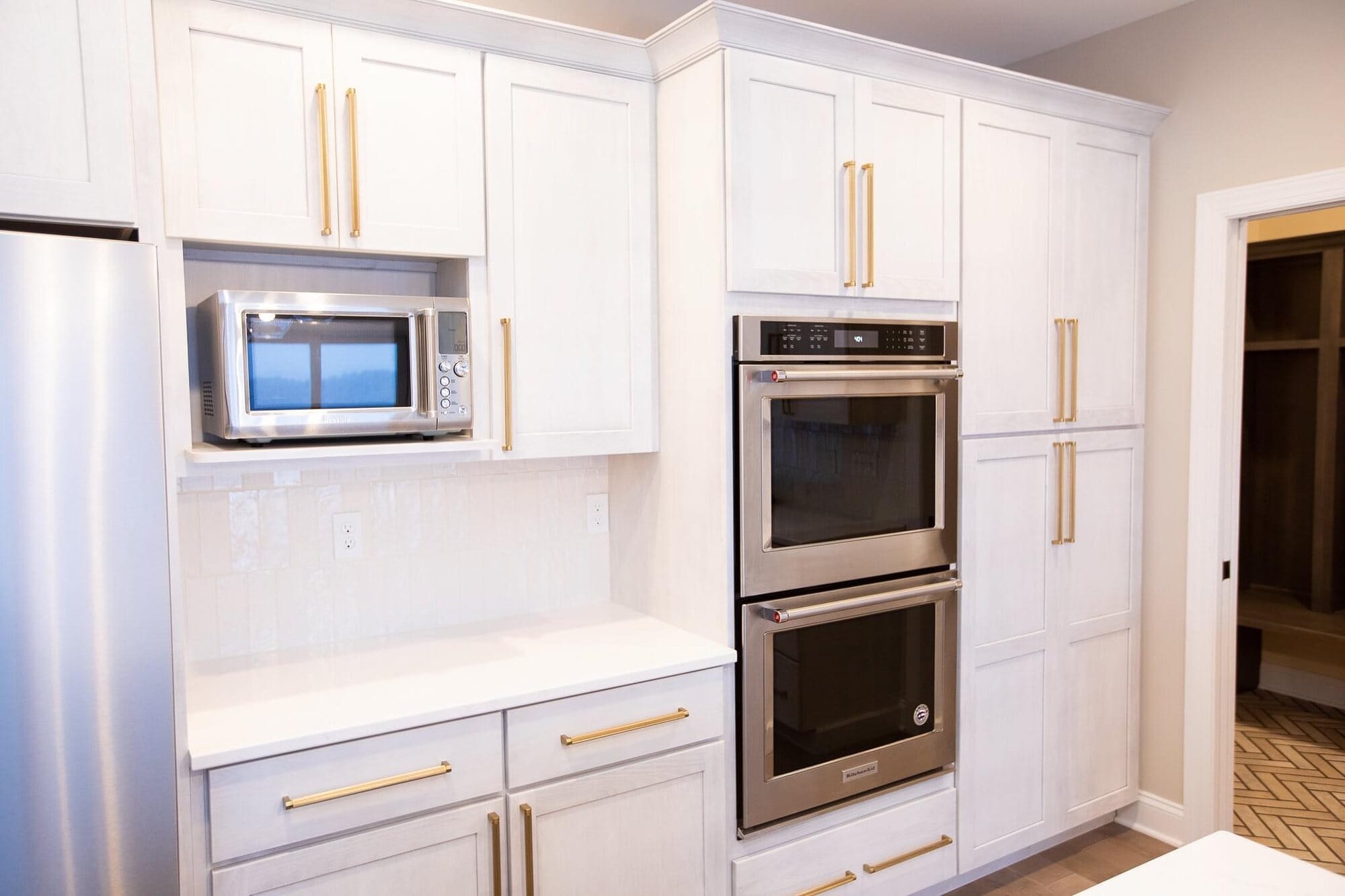 White kitchen detail with brushed gold hardware, a built-in microwave cabinet, double wall ovens, and a coffee bar niche.