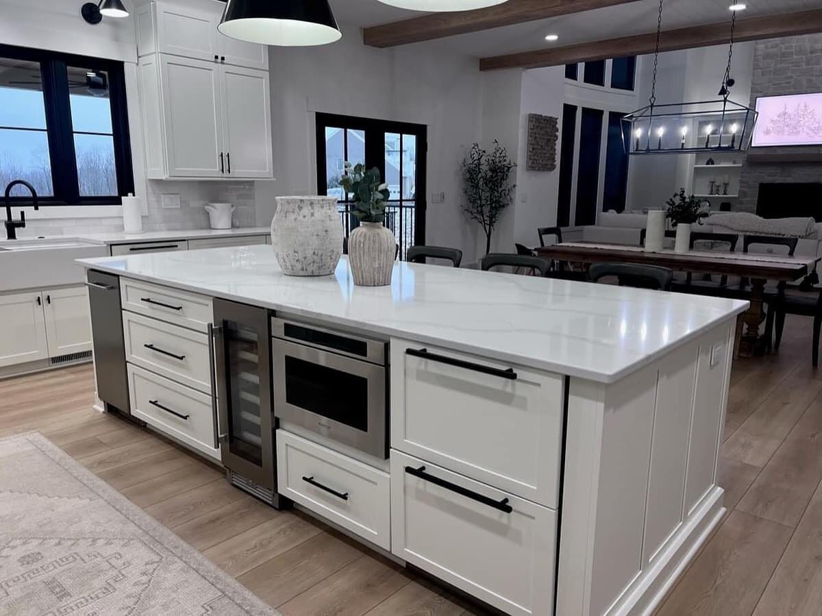 White kitchen island with a quartz waterfall top, built-in beverage refrigerator, microwave drawer, and open dining beyond.