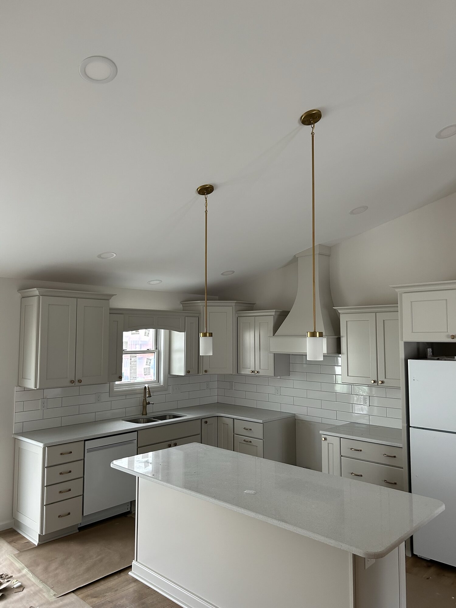 White kitchen with a vaulted ceiling, peninsula with quartz top, brass pendant lights, and stainless vent hood.